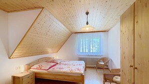 Ein Schlafzimmer mit schrägem Dach, einem Bett mit floralem Bettzeug, einem Korbsessel, einem Heizkörper und einem Holzschrank.