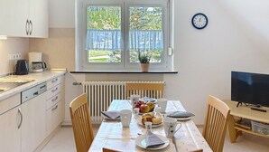 Eine moderne Küche mit einem Esstisch für zwei Personen, einer Kaffeemaschine und einem Fernseher auf einem Holzständer.