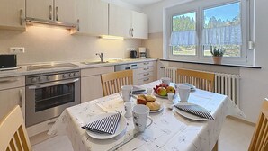 Eine moderne Küche mit Essbereich, ausgestattet mit Herd, Backofen, Spüle und einem Fenster mit Blick auf Grünflächen.