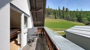 Eine Holzterrasse mit einem Stuhl, einem kleinen Tisch und Blick auf einen bewaldeten Hügel.