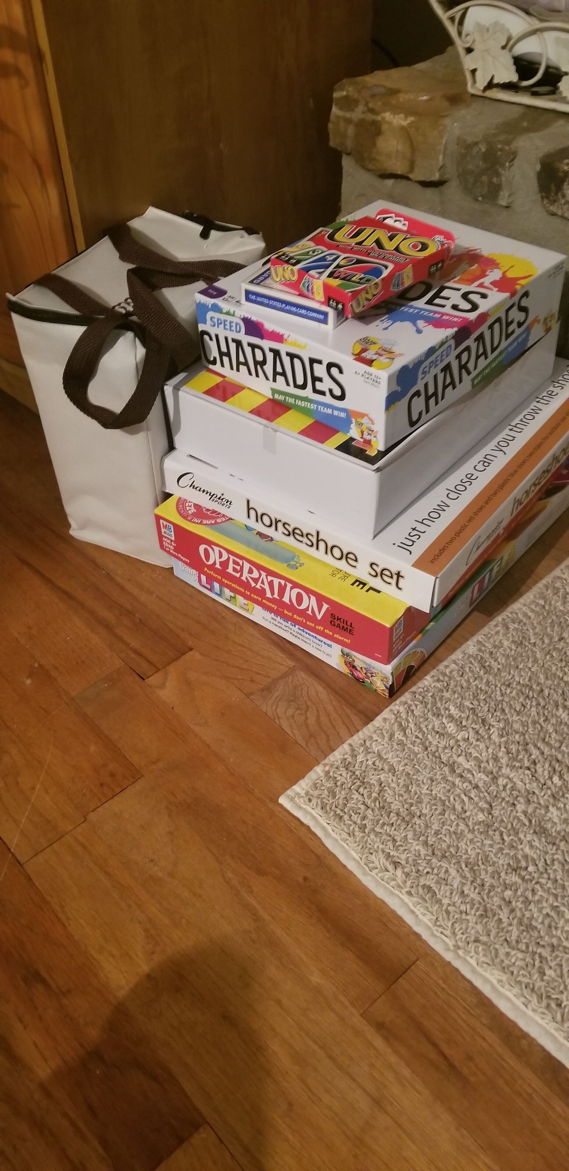 A stack of board games including UNO, Speed Charades, and Horseshoe Shoe Set on a wooden floor.
