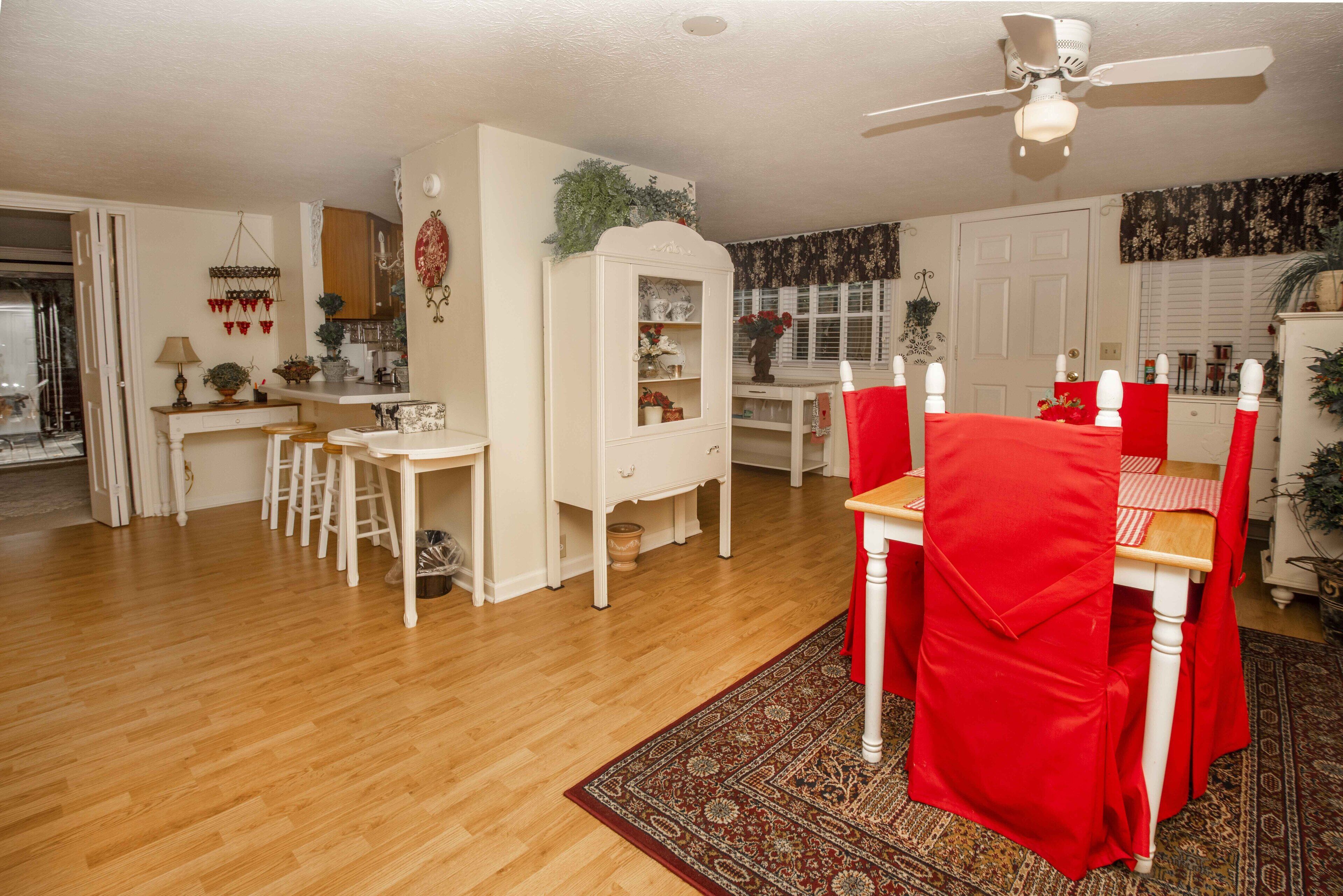 A dining area with a red table and chairs, a white cabinet, and a ceiling fan.