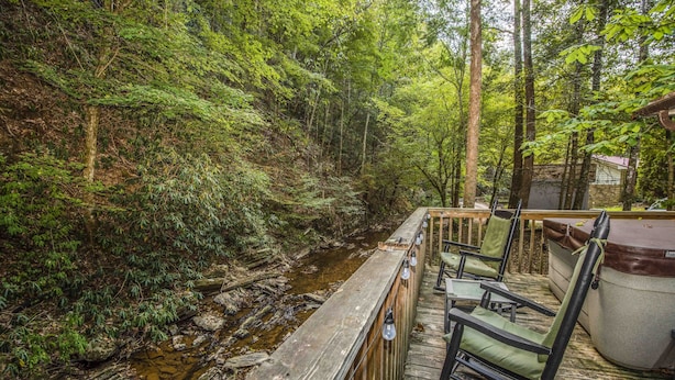 Une terrasse en bois, agrémentée de chaises, donnant sur un ruisseau au cœur d’une zone boisée.