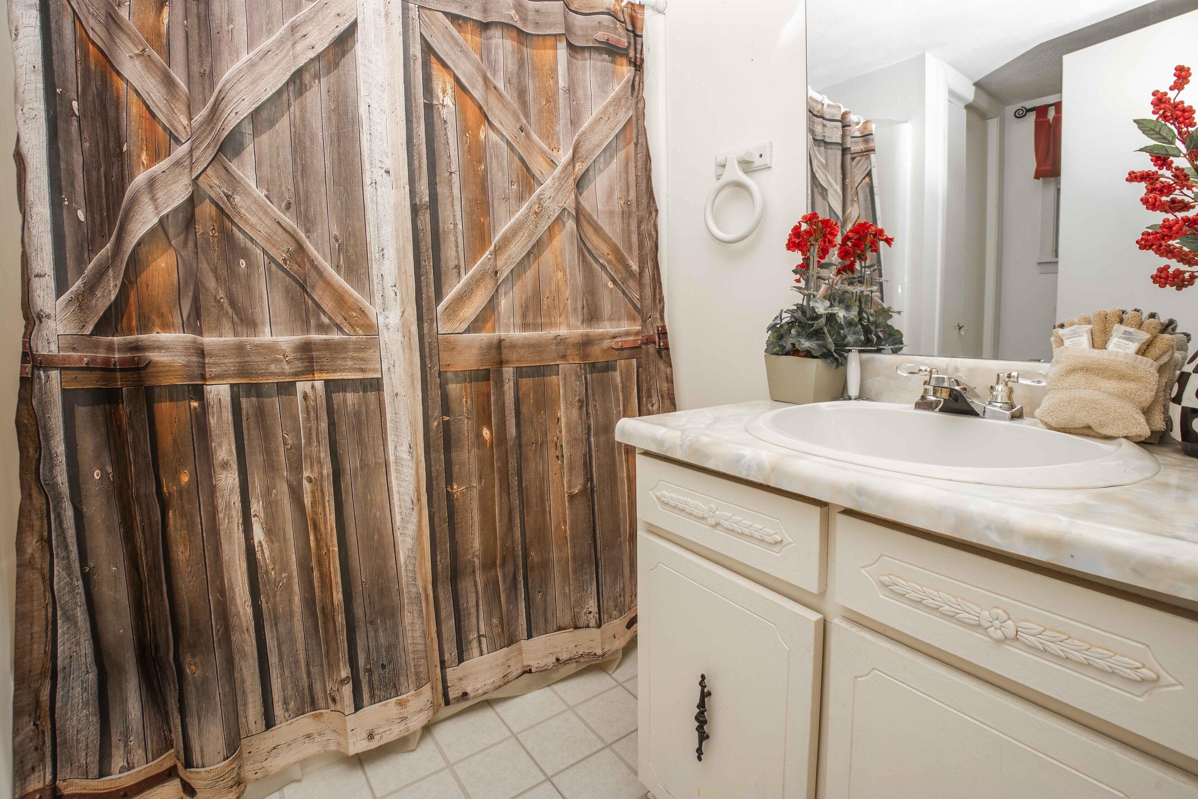 Une salle de bain avec une porte en bois rustique, un lavabo blanc et un miroir décoré de fleurs rouges.