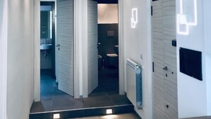 Un pasillo moderno con suelo de madera, paredes blancas y una puerta que da a un baño.