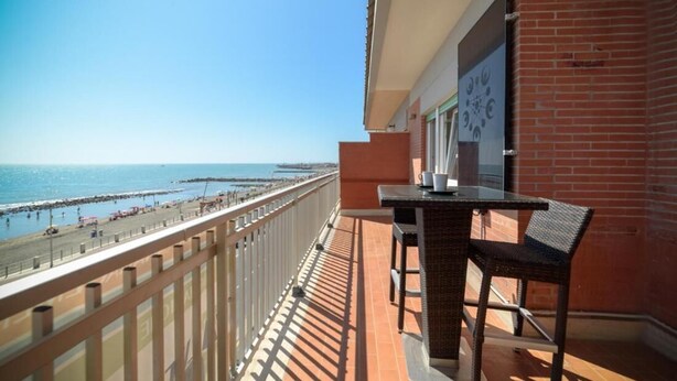 Un balcón con vista a la playa, una mesa con sillas y un muro de ladrillo.