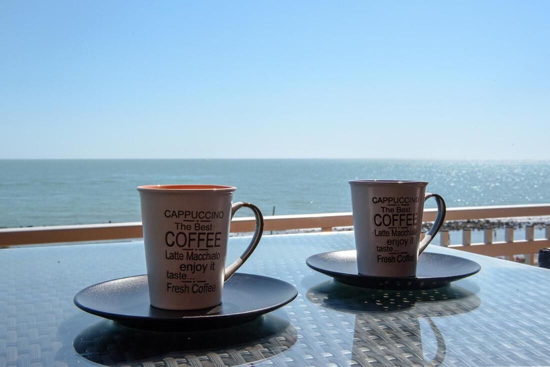 Two cappuccino cups with text on a table with a view of the sea.