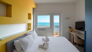 Habitación de hotel con cama, escritorio, televisor y balcón con vista al mar.