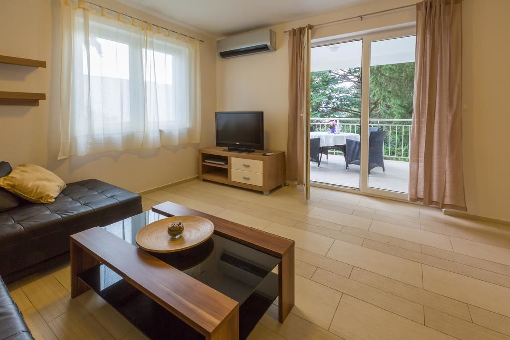 Una sala de estar moderna con sofá, mesa de centro, televisor sobre un mueble de madera y un balcón con mobiliario exterior.
