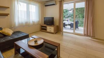 Una sala de estar moderna con sofá, mesa de centro, televisor sobre un mueble de madera y un balcón con mobiliario exterior.