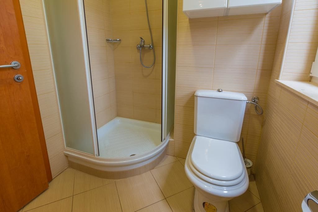 Un baño con inodoro, cabina de ducha y un mueble sobre el inodoro.