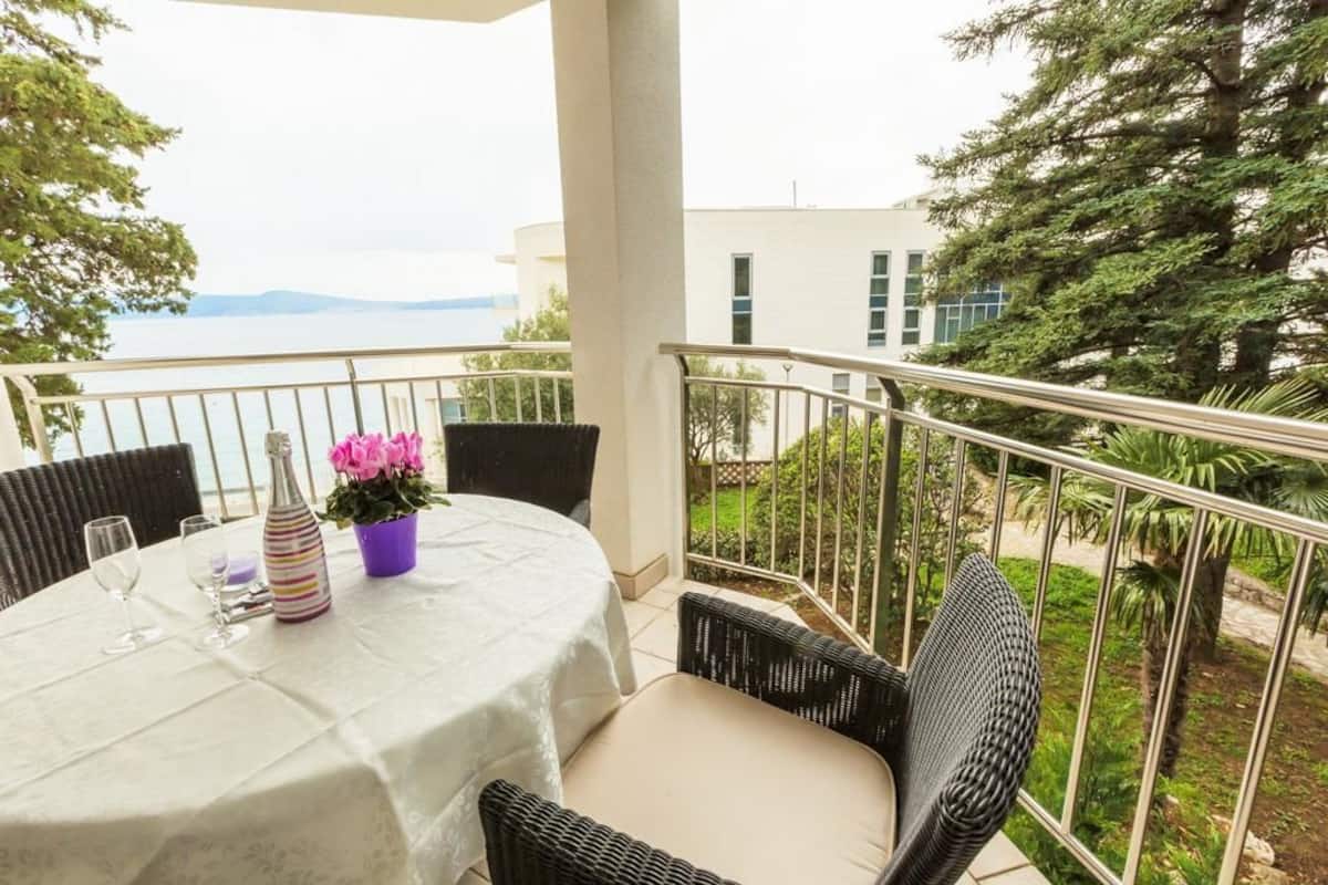 Un balcon avec une table dressée pour deux personnes, donnant sur une étendue d’eau et un bâtiment.