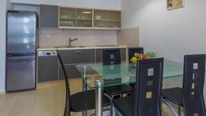 A modern kitchen with a stainless steel refrigerator, a glass-top dining table, and black chairs. - Apartmani Heta (Crikvenica)