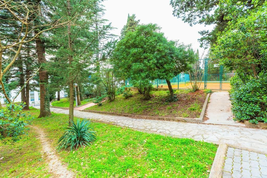 A pathway leading through a park-like area with trees and a sports field in the background.