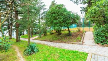 A pathway leading through a park-like area with trees and a sports field in the background.