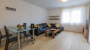 A modern living room with a glass dining table, black leather sofa, wooden coffee table, and a TV stand. - Apartmani Heta (Crikvenica)