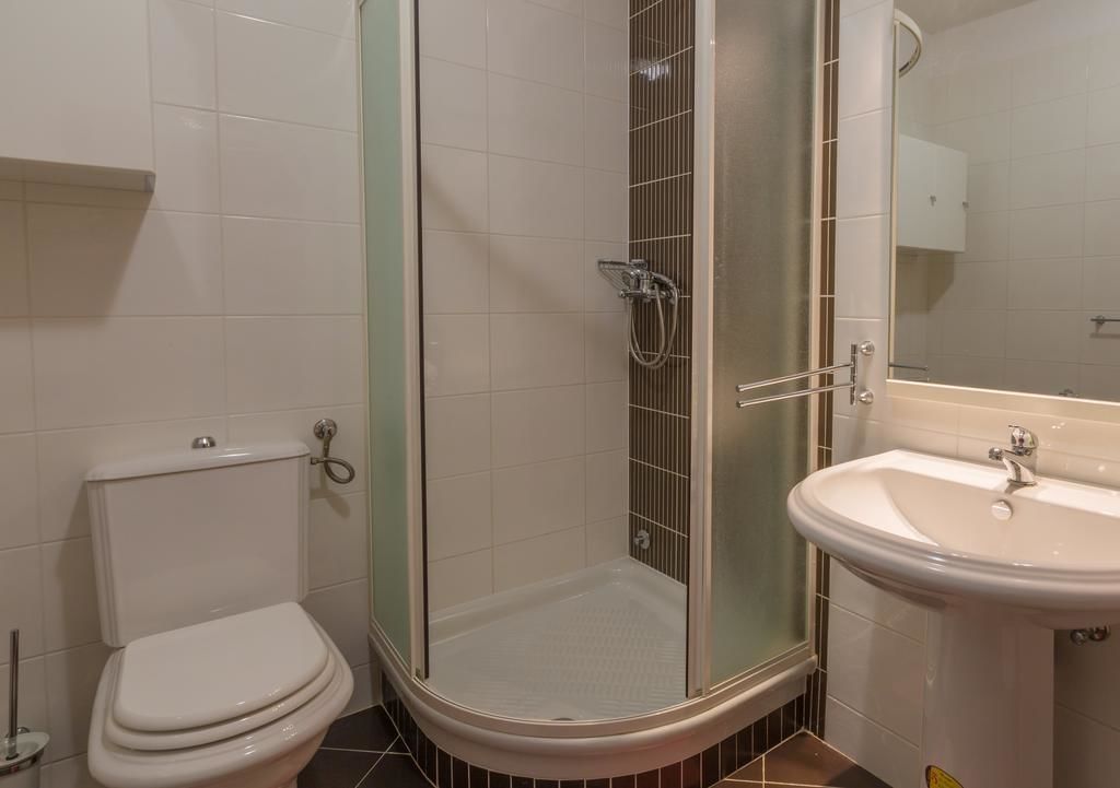 Un baño con inodoro, ducha con puerta de vidrio y lavamanos con espejo.