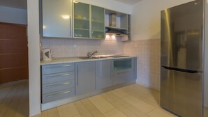A modern kitchen with a stainless steel refrigerator, grey cabinets, and a tiled backsplash. - Apartmani Heta (Crikvenica)