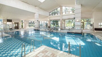 Una piscina interior con agua cristalina, paredes de azulejos y un interior iluminado por el sol.