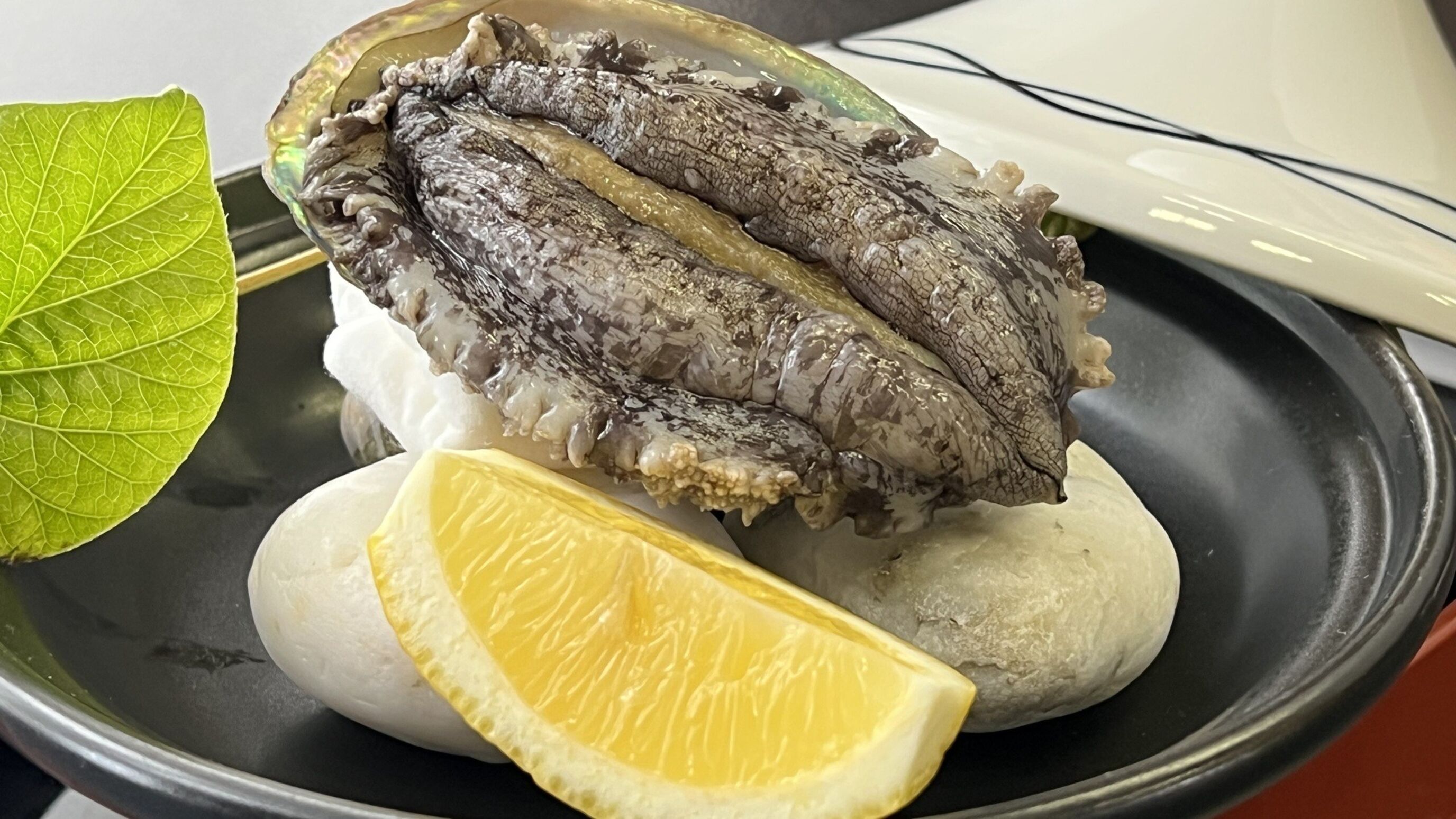 A dish with fish, lemon, and a green leaf on a plate.