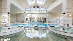 A large indoor swimming pool with multiple hot tubs, a central fountain, and a skylight ceiling. - Kurhouse Shirahama (Shirahama)