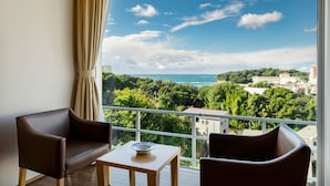 A balcony with two brown leather chairs and a small table, overlooking a coastal cityscape with greenery and buildings. - Kurhouse Shirahama (Shirahama)