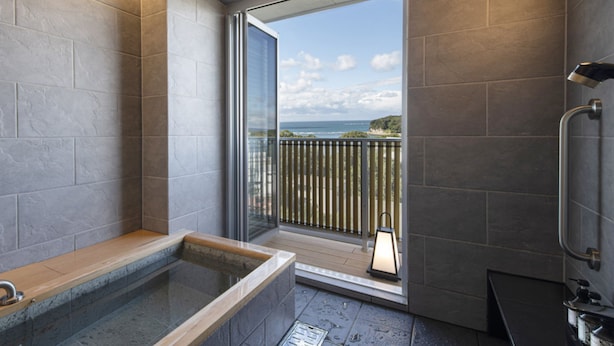 A bathroom with a bathtub, a shower, and a view of the ocean. - Kurhouse Shirahama (Shirahama)