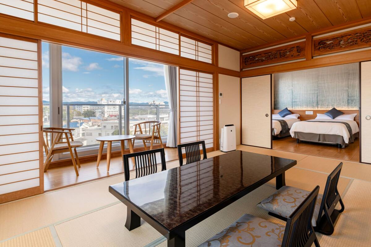 Ein traditioneller japanischer Raum mit Tatami-Böden, einem Holztisch und Blick auf die Stadt durch große Fenster.