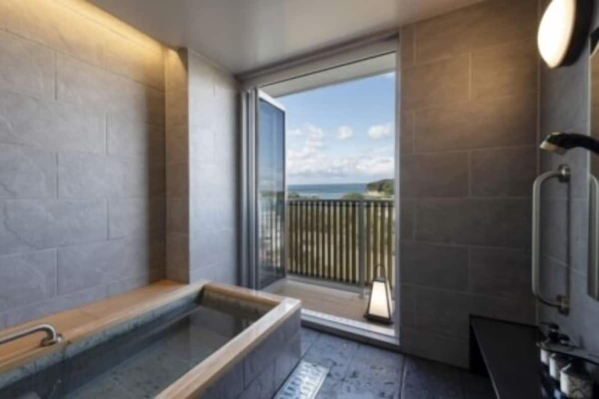 Ein modernes Badezimmer mit freistehender Badewanne, einer Duschkabine aus Glas und Meerblick durch ein großes Fenster.