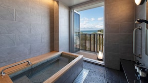 A modern bathroom with a glass-enclosed shower, a wooden bench, and a view of the sea. - Kurhouse Shirahama (Shirahama)