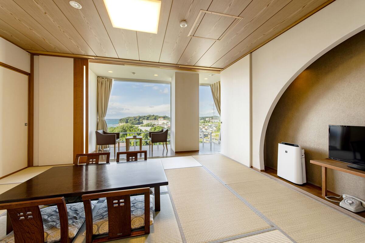 Ein geräumiges Zimmer mit einem großen Esstisch, Stühlen, einem Fernseher und Blick auf die Stadt.