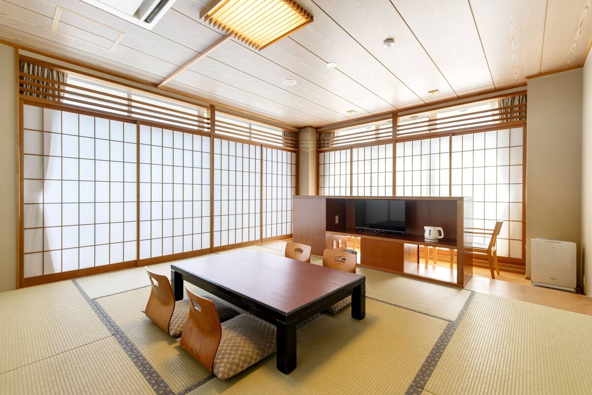Ein traditioneller japanischer Raum mit Tatami-Boden, einem niedrigen Tisch und verschiebbaren Türen.