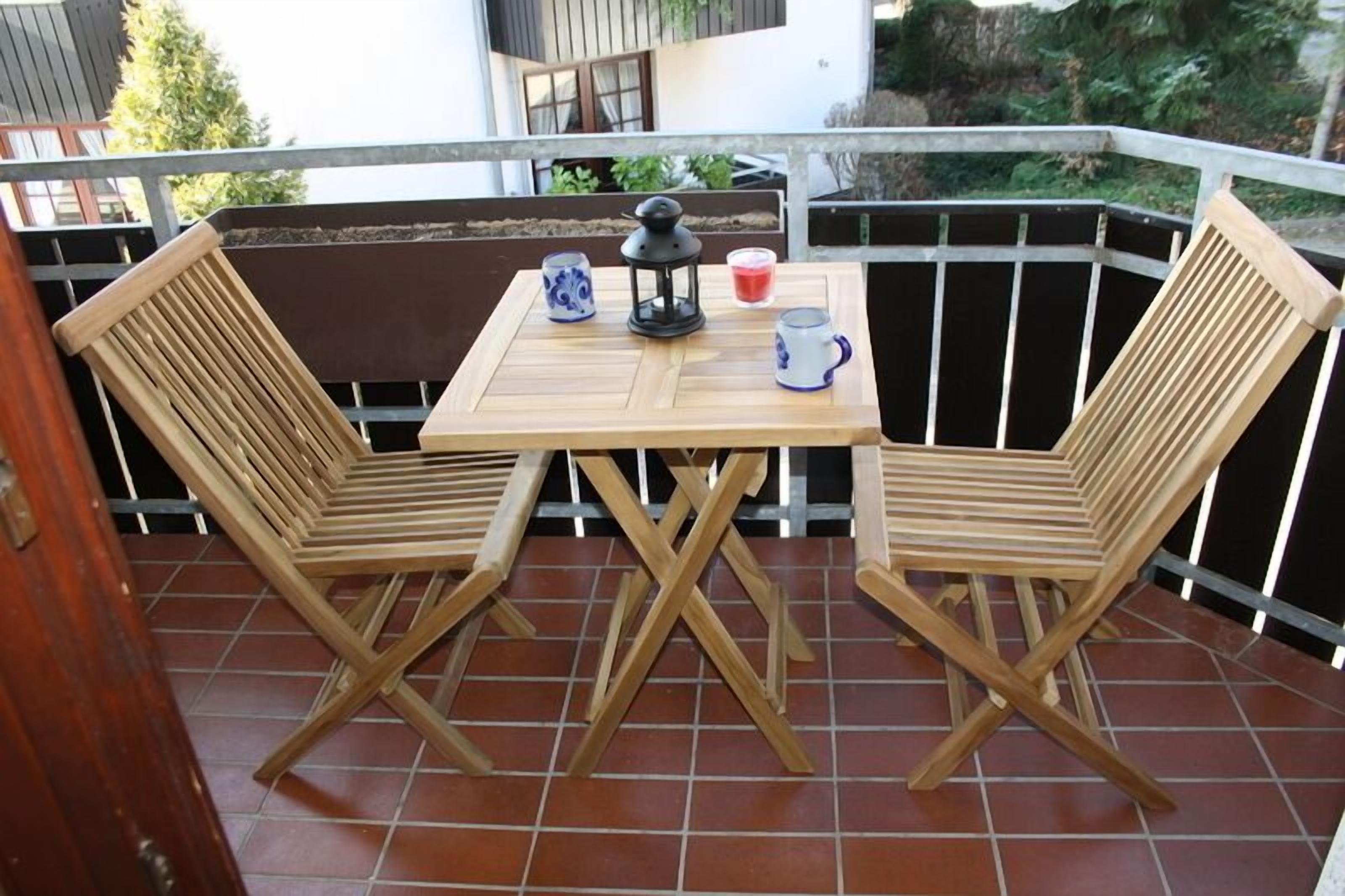 A wooden table with two chairs on a balcony with a railing.