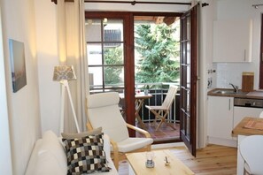 Une pièce confortable avec un canapé, un fauteuil, une table et une vue sur un balcon comprenant un coin repas et une cuisine.