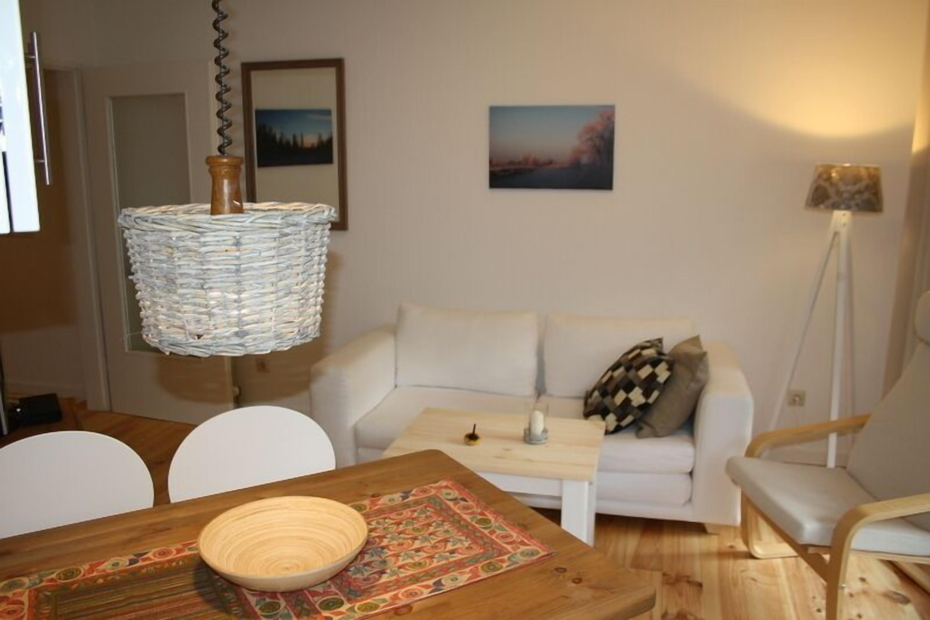 Ein modernes Wohnzimmer mit einem weißen Sofa, einem Holzespeisetisch mit Stühlen, einer Pendelleuchte und einem kleinen Beistelltisch mit Kerze.
