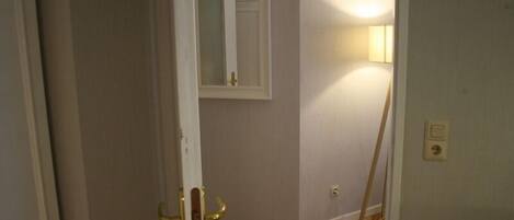 A room with a wooden floor, a white door, a mirror on the wall, and a standing lamp.