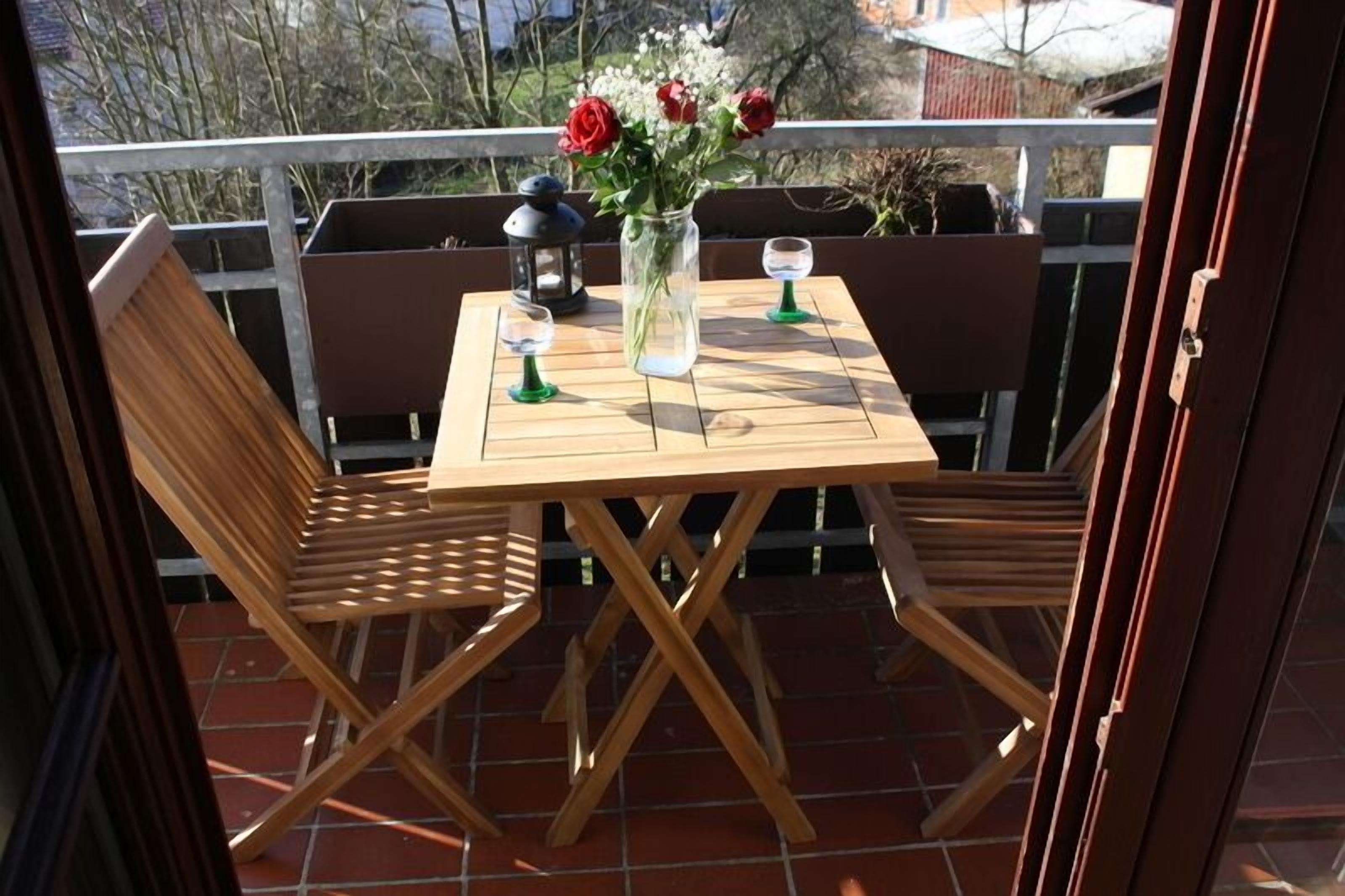 A wooden table with two chairs on a balcony, a vase with flowers, and two lanterns.