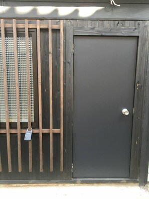 A dark wooden door with a metal security lock and a metal gate with vertical bars. - nid Tani6 House (Osaka)