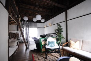 A compact, modern room with a bunk bed, a green storage unit, a black chair, a sofa, and a large potted plant. - nid Tani6 House (Osaka)
