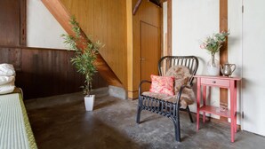 A room with a wooden ceiling, a black wicker chair with a red cushion, a white potted plant, and a small pink table with a vase and a silver pitcher. - nid Tani6 House (Osaka)