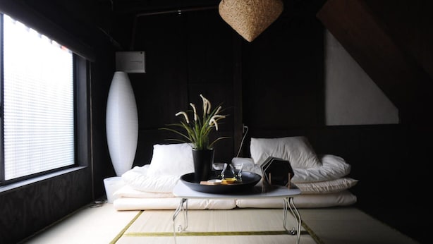 A modern living room with a tatami mat floor, a low sofa, a coffee table, a potted plant, and a hanging light fixture. - nid Tani6 House (Osaka)