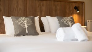 A neatly made bed with white and gray pillows, a wooden headboard, and a wall-mounted light fixture. - The Cross Keys (Knutsford)