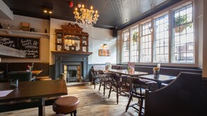 A cozy restaurant with wooden furniture, a fireplace, and large windows. - The Cross Keys (Knutsford)