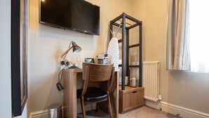 A corner room with a desk, chair, television, ironing board, radiator, and a window with curtains. - The Cross Keys (Knutsford)
