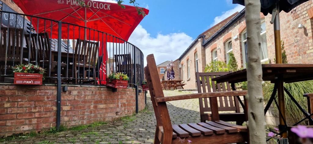 Un parapluie rouge orné du logo « PIMMS », un mur de briques et un banc en bois.