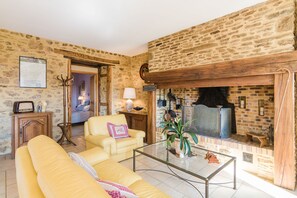 Un salon chaleureux avec un mur en pierre, une cheminée, un canapé jaune et une table basse en verre.