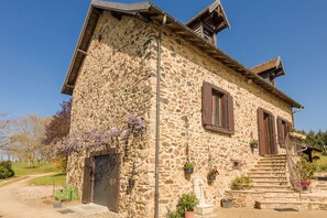 Un bâtiment en pierre avec un toit en pente, des volets en bois et un petit escalier menant à l’entrée.
