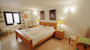 Ein helles Schlafzimmer mit einem hölzernen Bett, Nachttischen mit Lampen, einem Sessel und Bildern an den Wänden.