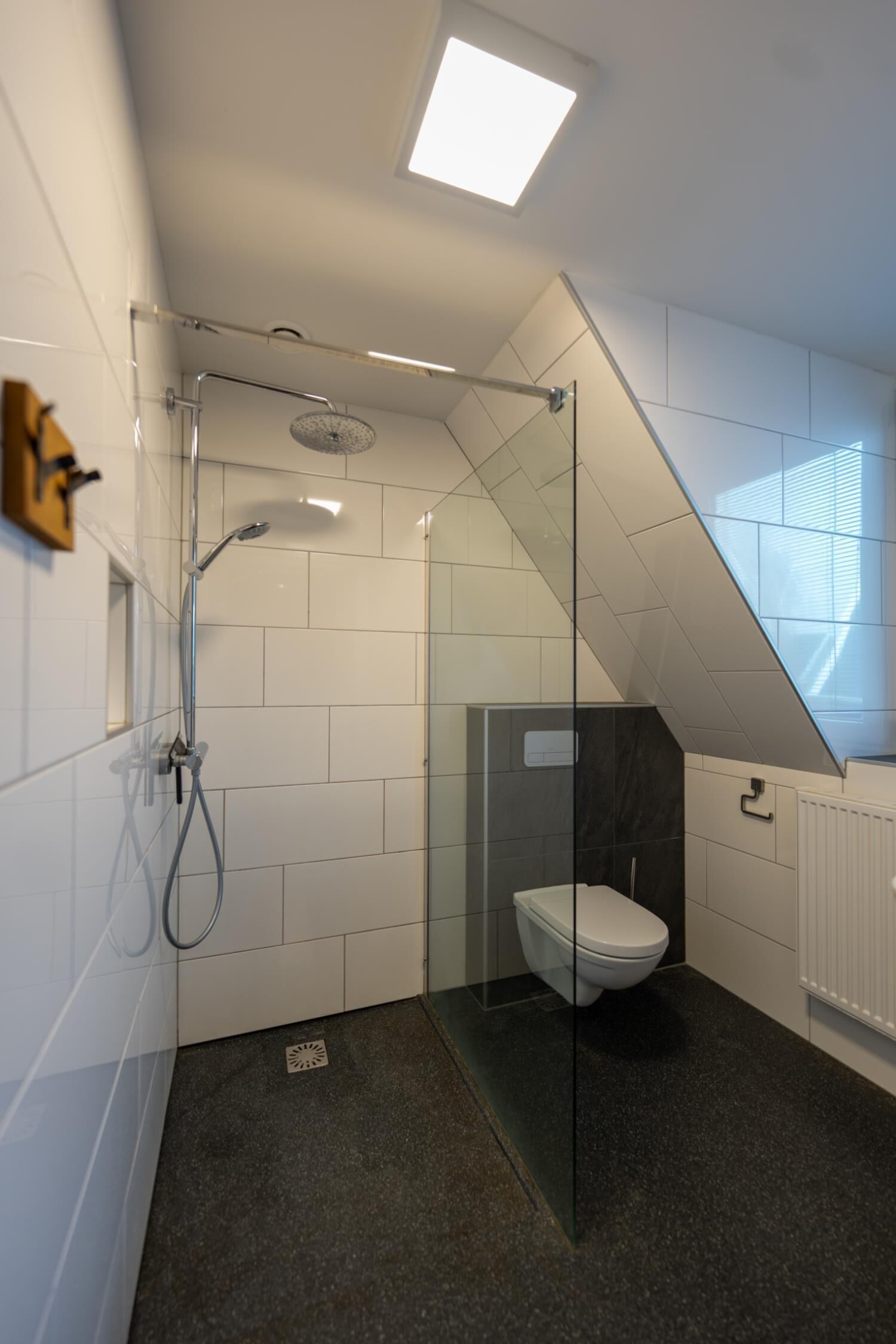 A modern bathroom with a glass shower enclosure, white tiles, and a dark floor.