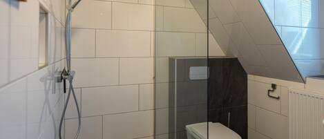 A modern bathroom with a glass shower enclosure, white tiles, and a dark floor.